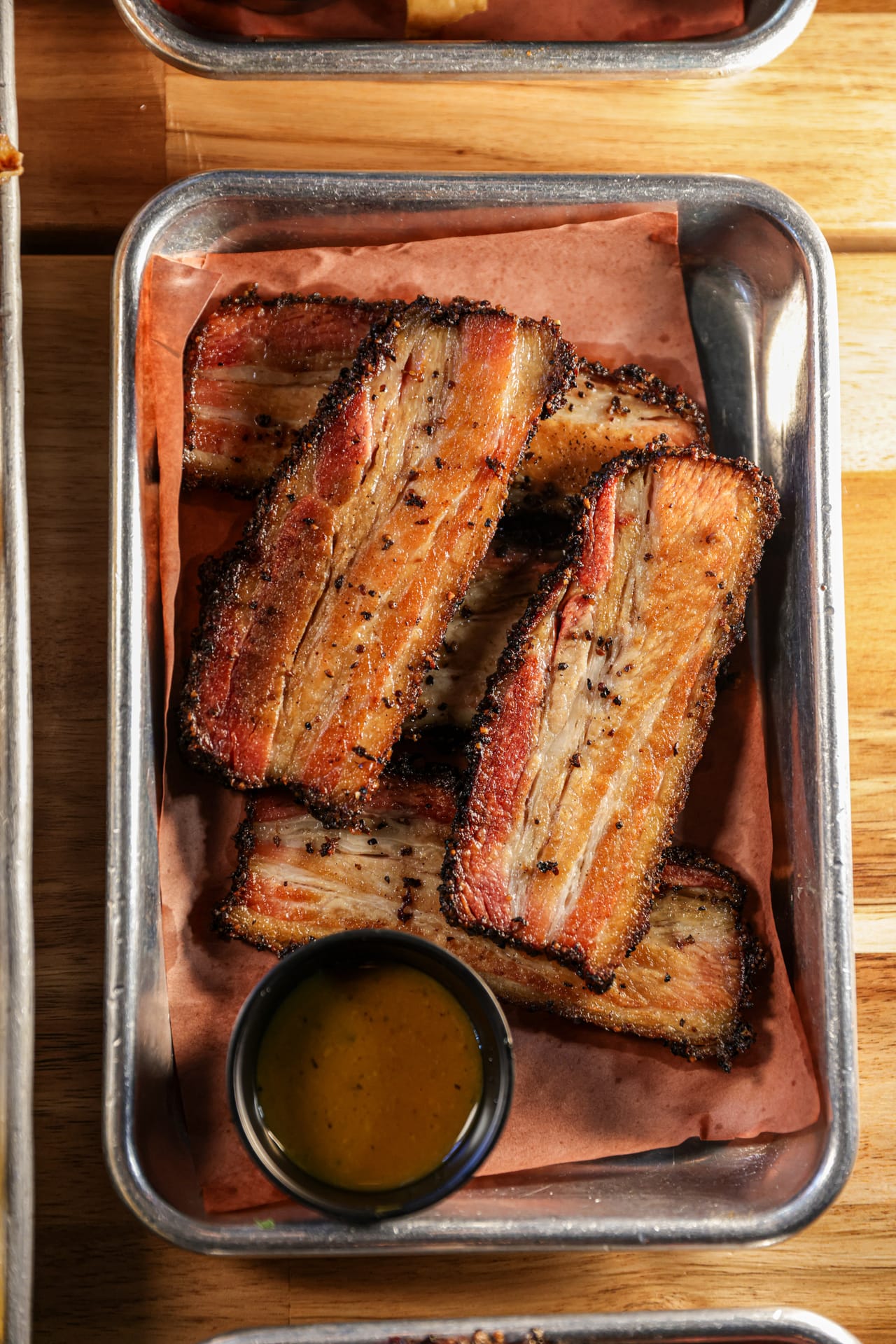 Thick slices of smoked brisket bacon with a peppered bark on a steel tray at Apocalypse BBQ Miami